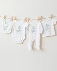 A collection of baby clothes, including onesies and bibs, hanging on a clothesline.