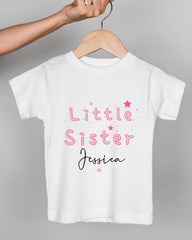 A white t-shirt with pink text and stars printed on it, being held by a person's hand.
