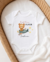 A white onesie with a cartoon bear and airplane printed on it, placed on a white blanket.