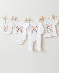 A collection of baby clothes, including onesies and bibs, hanging on a clothesline.