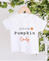 A white t-shirt with the text "Little Pumpkin Emily" printed on it, hanging on a wooden hanger.