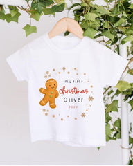 A white t-shirt with a gingerbread man graphic and text that says "My first christmas Oliver" and "20x".