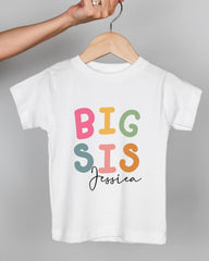 A person's hand is holding a white t-shirt with the text "BIG SIS Jessica" printed on it.