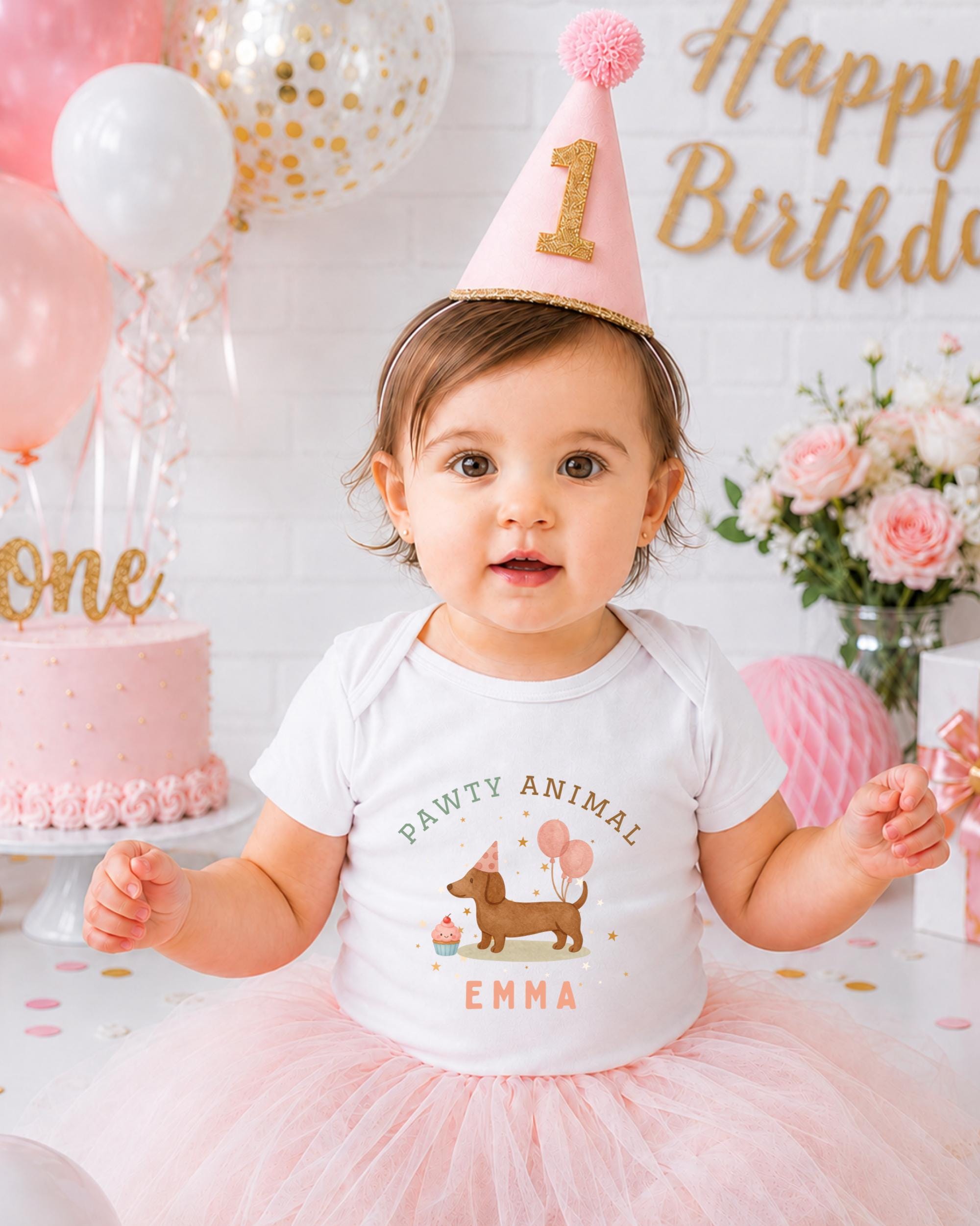 A young girl wearing a birthday hat and a white t-shirt with a dog design is posing in front of a birthday cake and balloons.