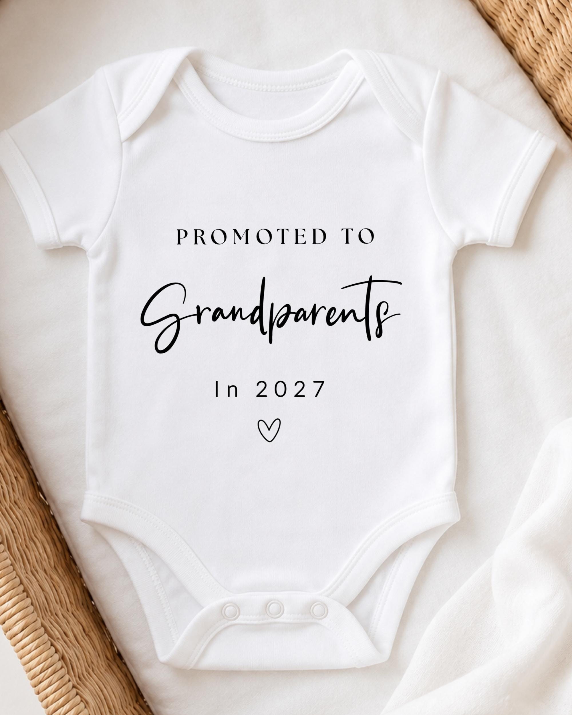 A white baby onesie with text printed on it, placed on a white surface.