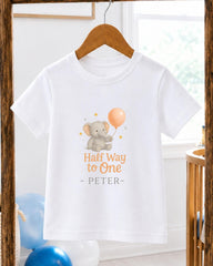 A white t-shirt with a graphic design featuring a gray elephant holding a balloon, along with the text "Half Way to One - PETER".