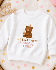 A white sweatshirt with a teddy bear and birthday text printed on it, surrounded by confetti.