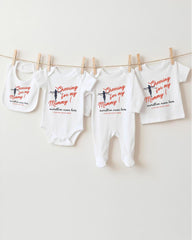 A row of baby clothes, including onesies and bibs, hanging on a clothesline.