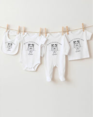 A collection of white baby clothes, including onesies and bibs, hanging on a clothesline.