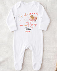 A white onesie with a printed design on it, featuring a teddy bear and the text "Up up away! First time flyer Jessica - 2026".