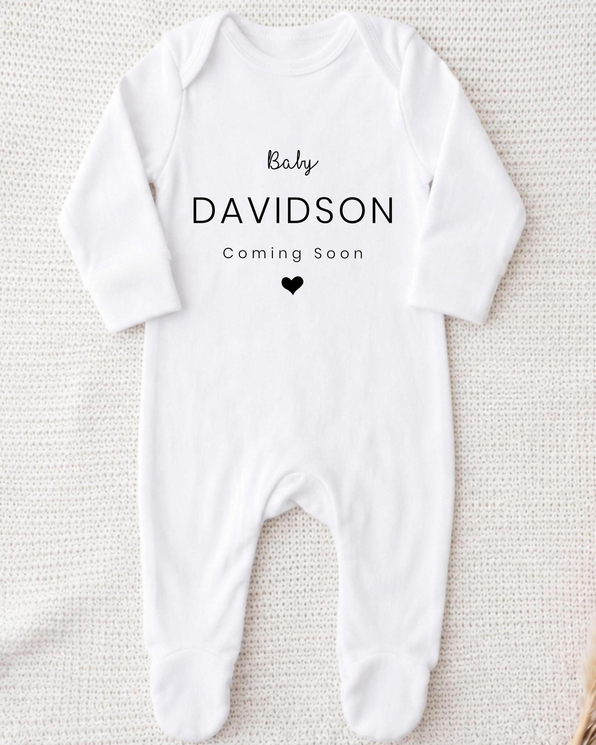 A white onesie with the text "Baby Davidson Coming Soon" printed on it.