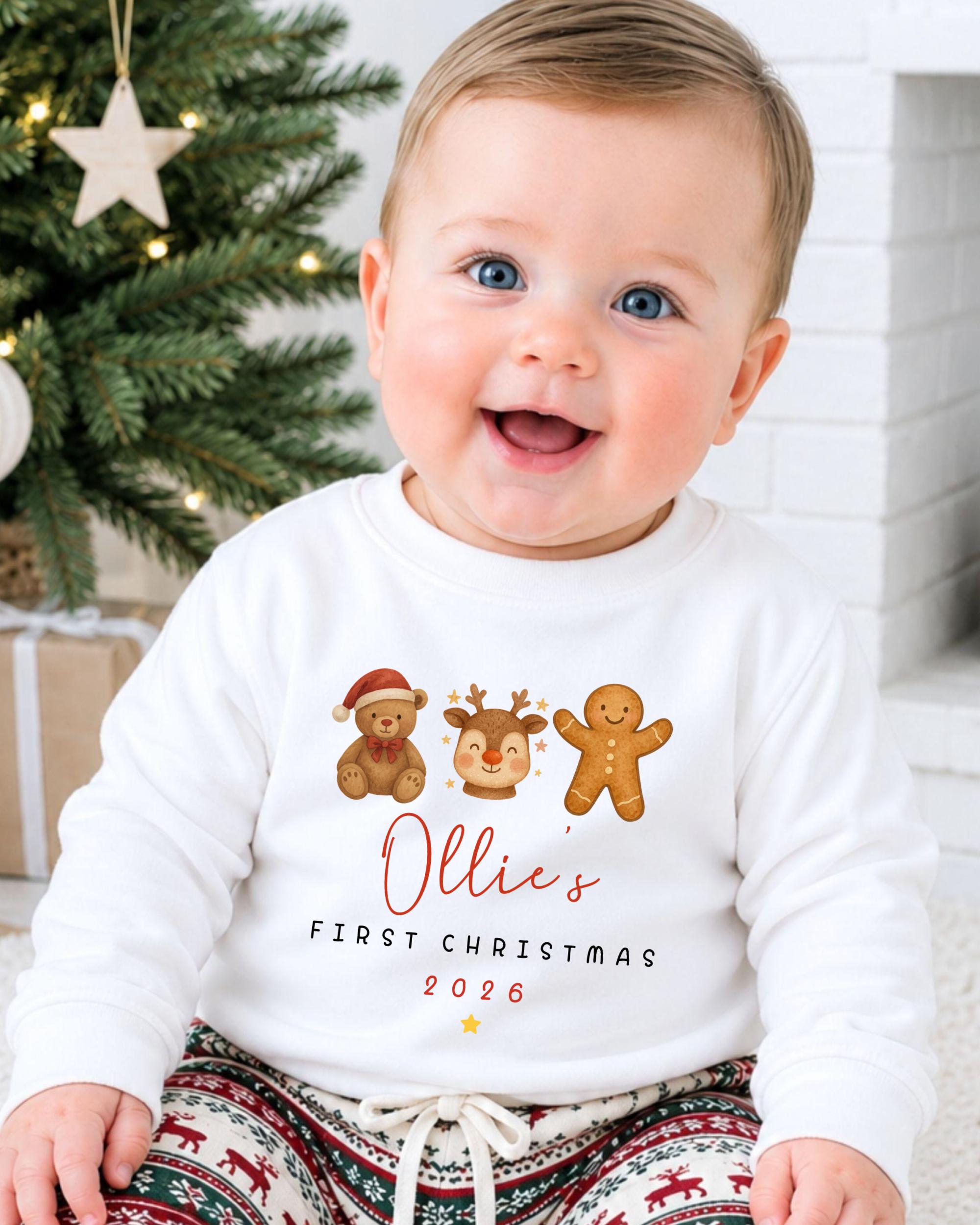 A smiling baby wearing a white sweater with a personalized Christmas-themed design, including a teddy bear, gingerbread man, and reindeer.