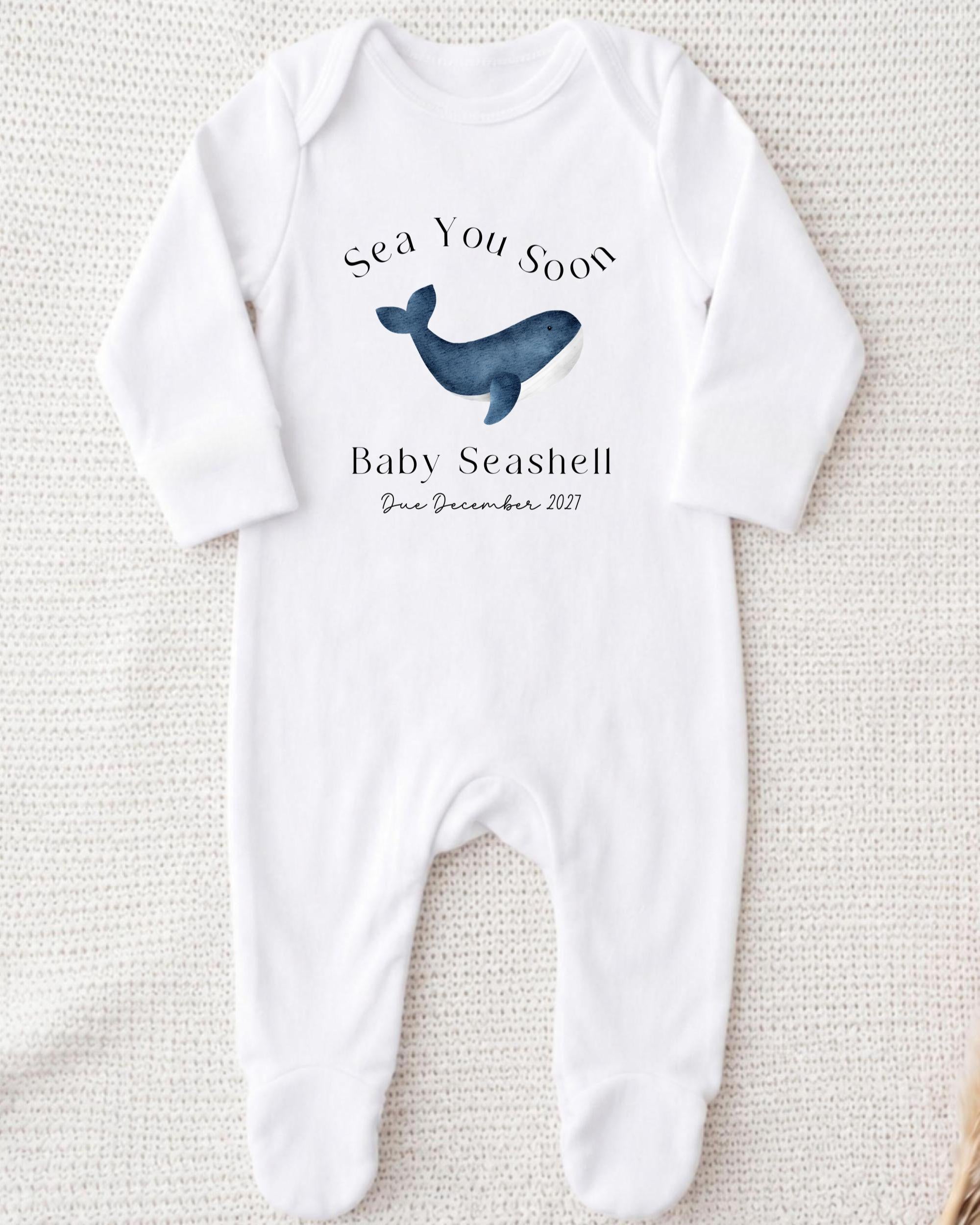 A white onesie with a graphic of a blue whale and text that reads "Sea You Soon Baby Seahell Due December 2021".