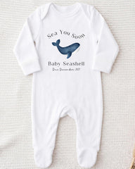 A white onesie with a graphic of a blue whale and text that reads "Sea You Soon Baby Seahell Due December 2021".