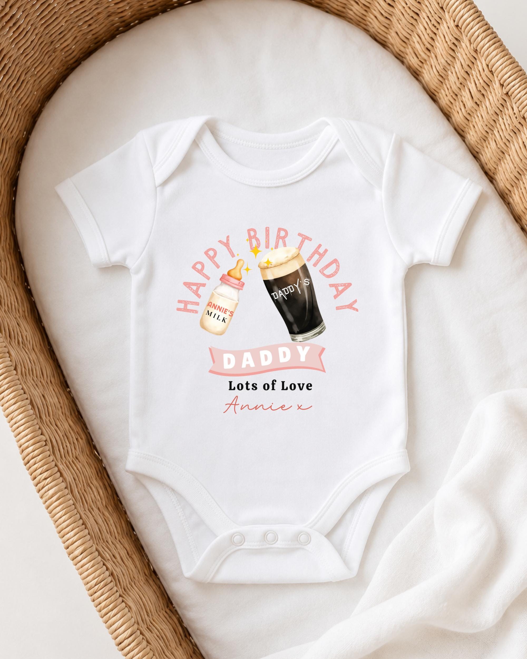 A white onesie with a graphic design on it, featuring a bottle of milk and a glass of beer, along with the text "Happy Birthday Daddy Lots of Love Annie".