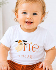 A smiling baby boy wearing a white t-shirt with a ghost and stars printed on it.