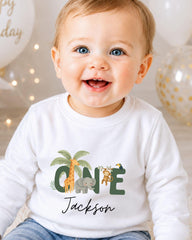 A smiling baby boy wearing a white shirt with a jungle-themed graphic and the name "Jackson" printed on it.