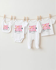 A row of four white baby clothes with the text "FIRST TIME FLYER Barcelona" printed on them, hanging on a clothesline.