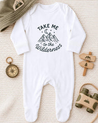 A white onesie with a mountain and star design, along with a compass, a hat, and a toy binoculars, all arranged on a beige surface.