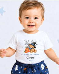 A smiling baby boy wearing a white t-shirt with a Halloween-themed design and a spider web.