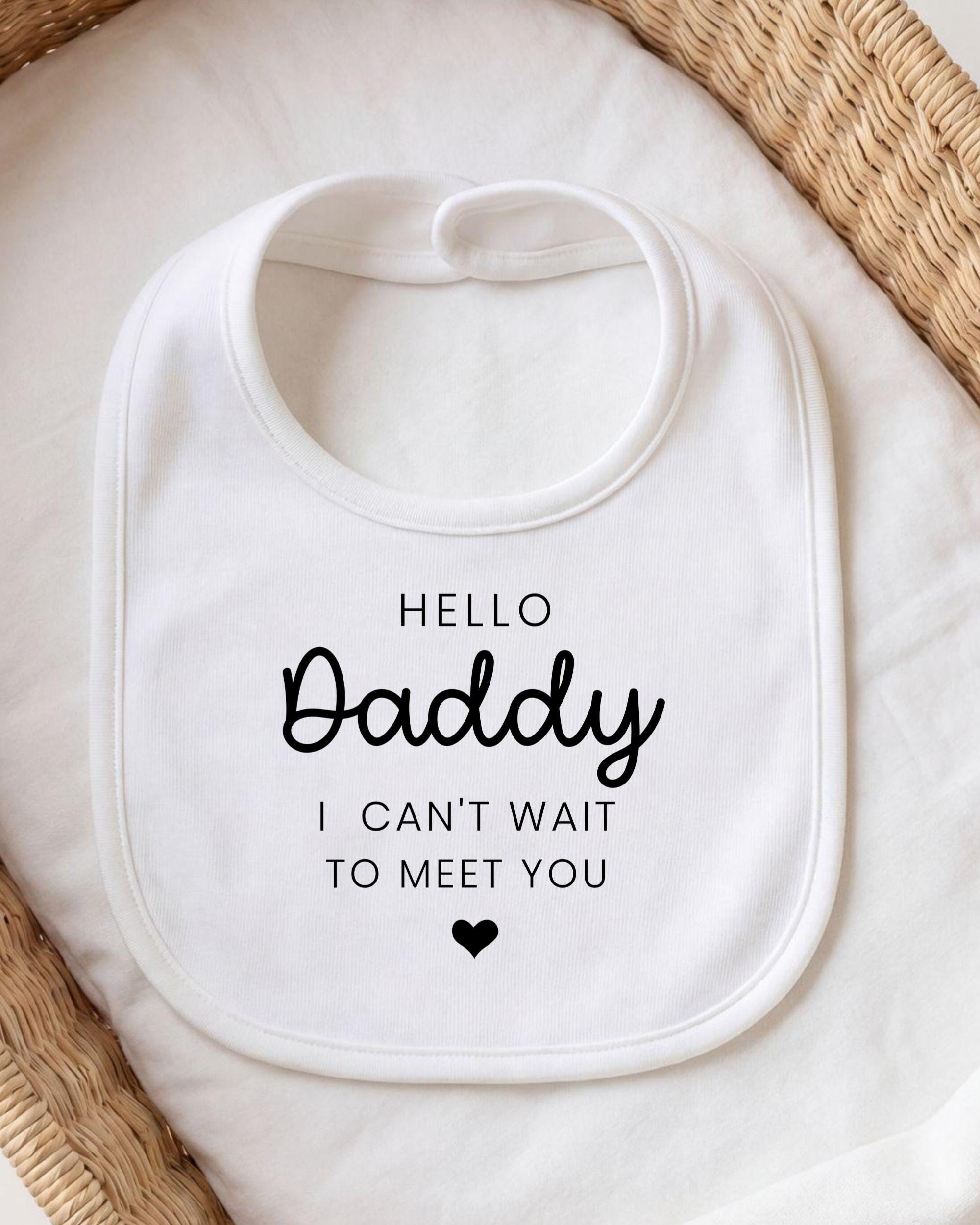 A white bib with the text "HELLO Daddy I CAN'T WAIT TO MEET YOU" printed on it.