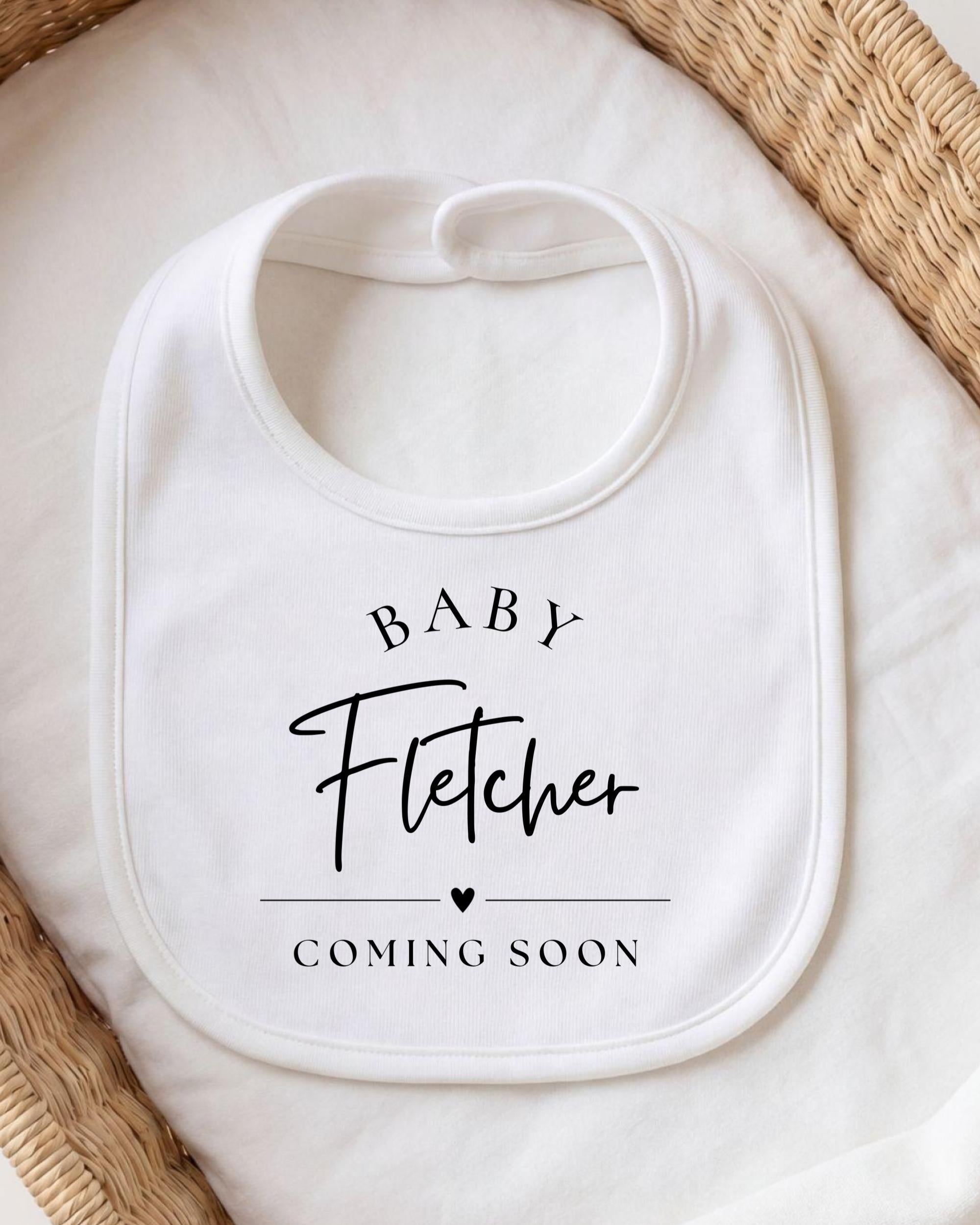A white baby bib with the text "BABY FLETCHER COMING SOON" printed on it.