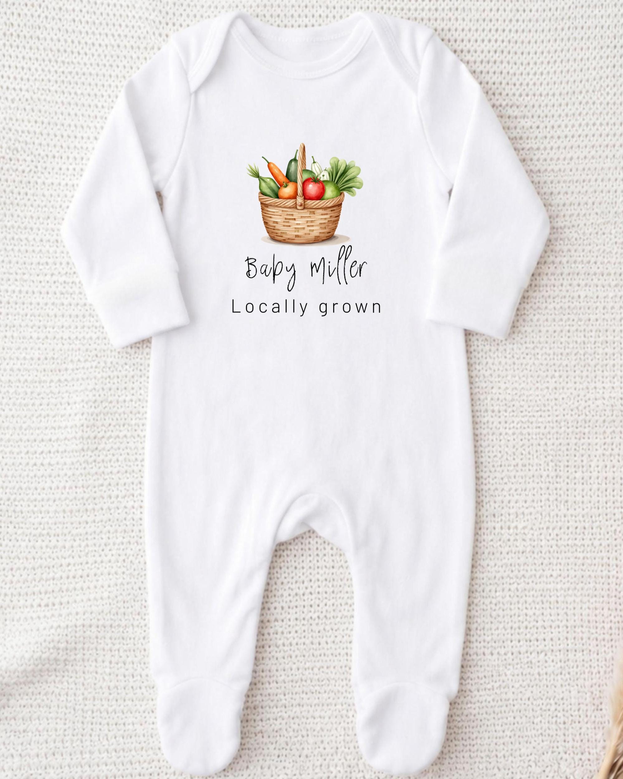 A white onesie with a printed image of a basket of vegetables and the text "Baby Miller Locally grown" printed on it.