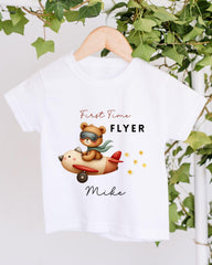 A white t-shirt with a cartoon image of a bear riding an airplane, along with the text "First Time Flyer Mike" printed on it.