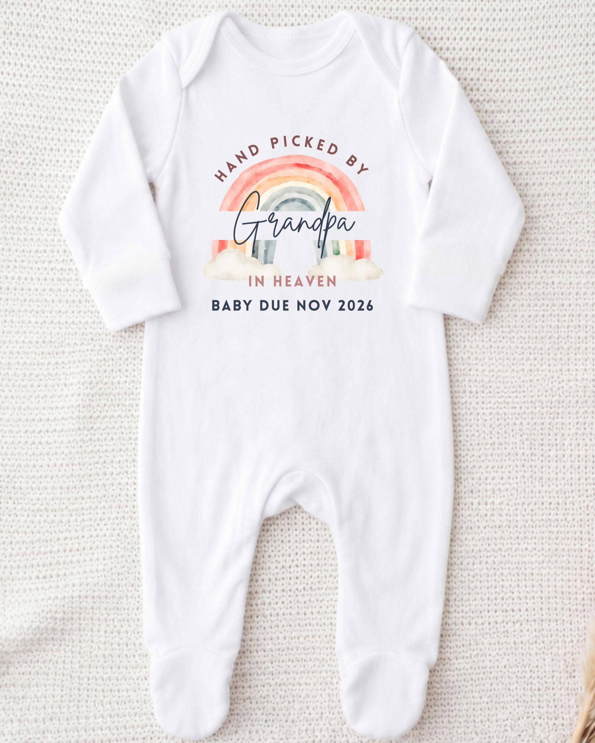 A white onesie with a graphic design on it, which says "Hand picked by Grandpa in Heaven Baby due Nov 2026".