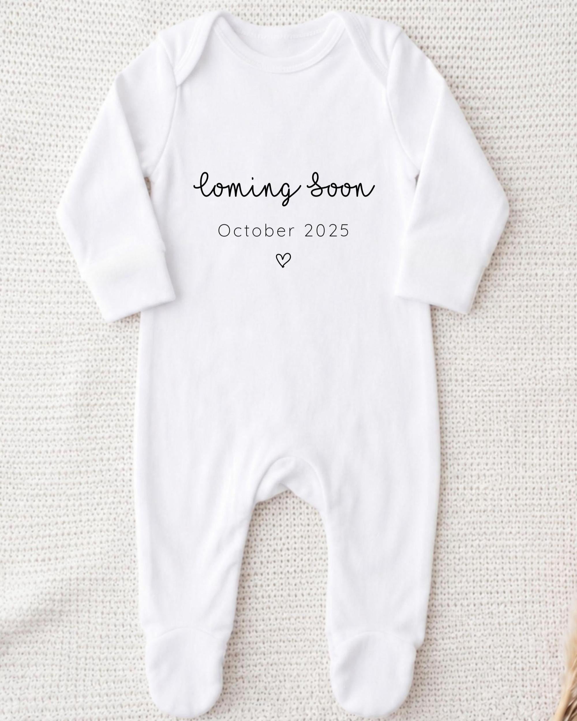 A white onesie with the text "Coming soon October 2025" printed on it.