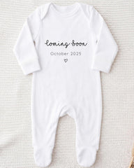 A white onesie with the text "Coming soon October 2025" printed on it.