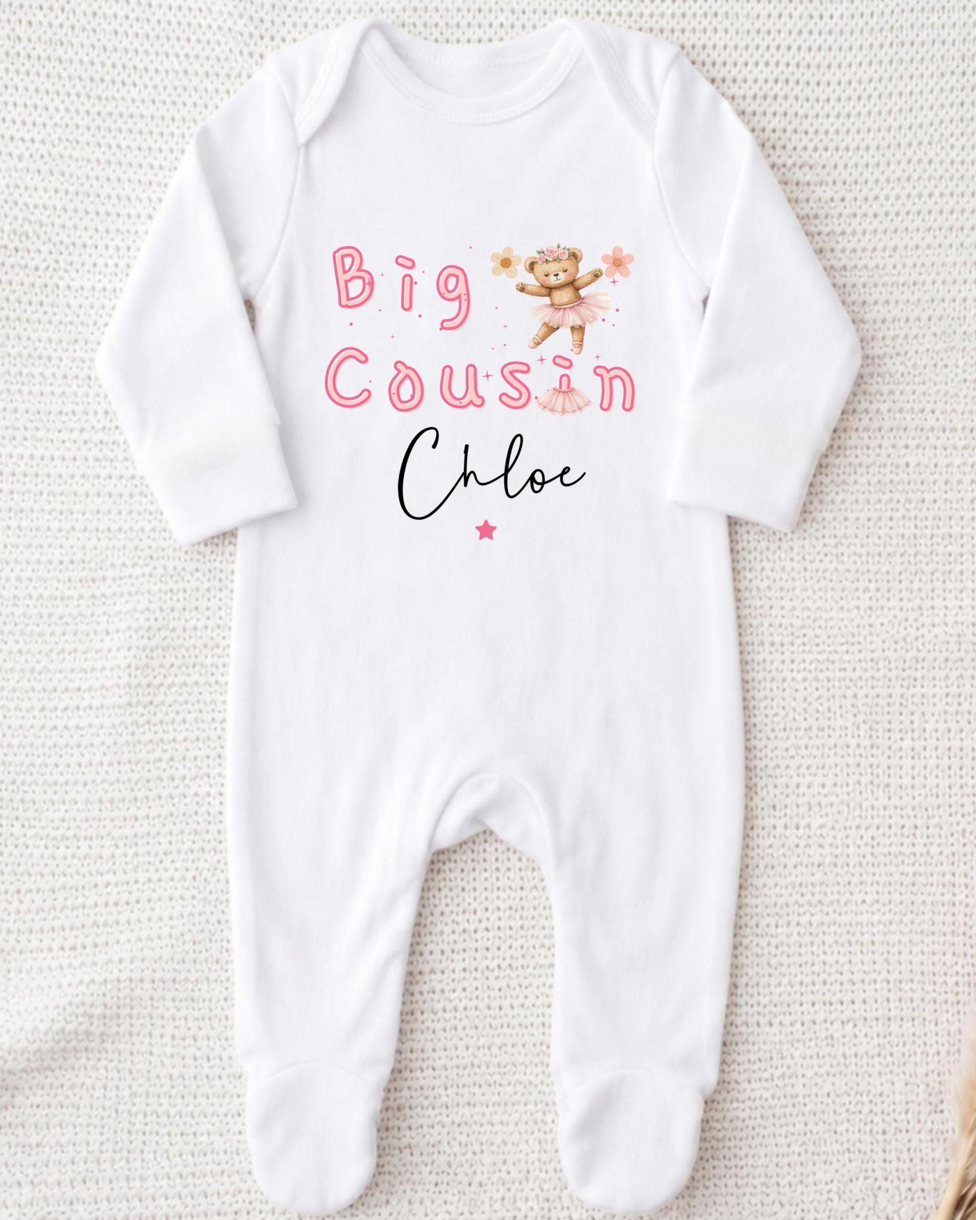 A white onesie with the text "Big Cousin Chloe" printed on it, along with a small illustration of a teddy bear.