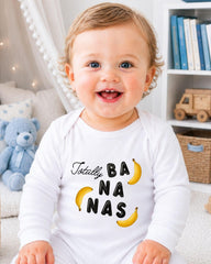 A smiling baby wearing a white onesie with the text "Totally BANANA NANA" printed on it.