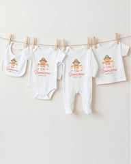 A row of four white baby clothes with a cartoon scarecrow design hanging on a clothesline.