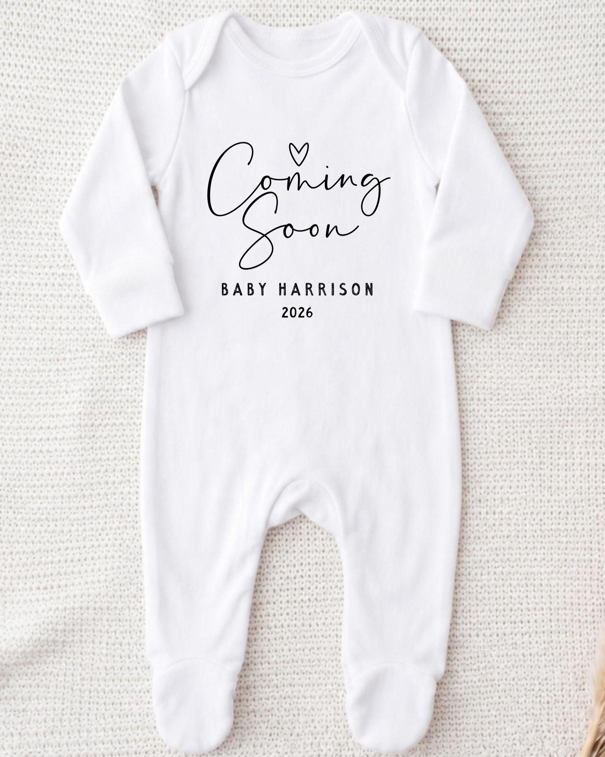 A white onesie with the text "Coming Soon" and "Baby Harrison 2026" printed on it.