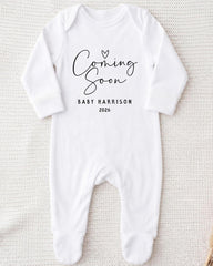 A white onesie with the text "Coming Soon" and "Baby Harrison 2026" printed on it.
