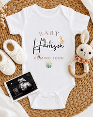 A baby announcement outfit with the name "Harison" printed on it, along with a crocheted rabbit toy and a baby bootie. There is also an Ultrasound image of a baby's belly.