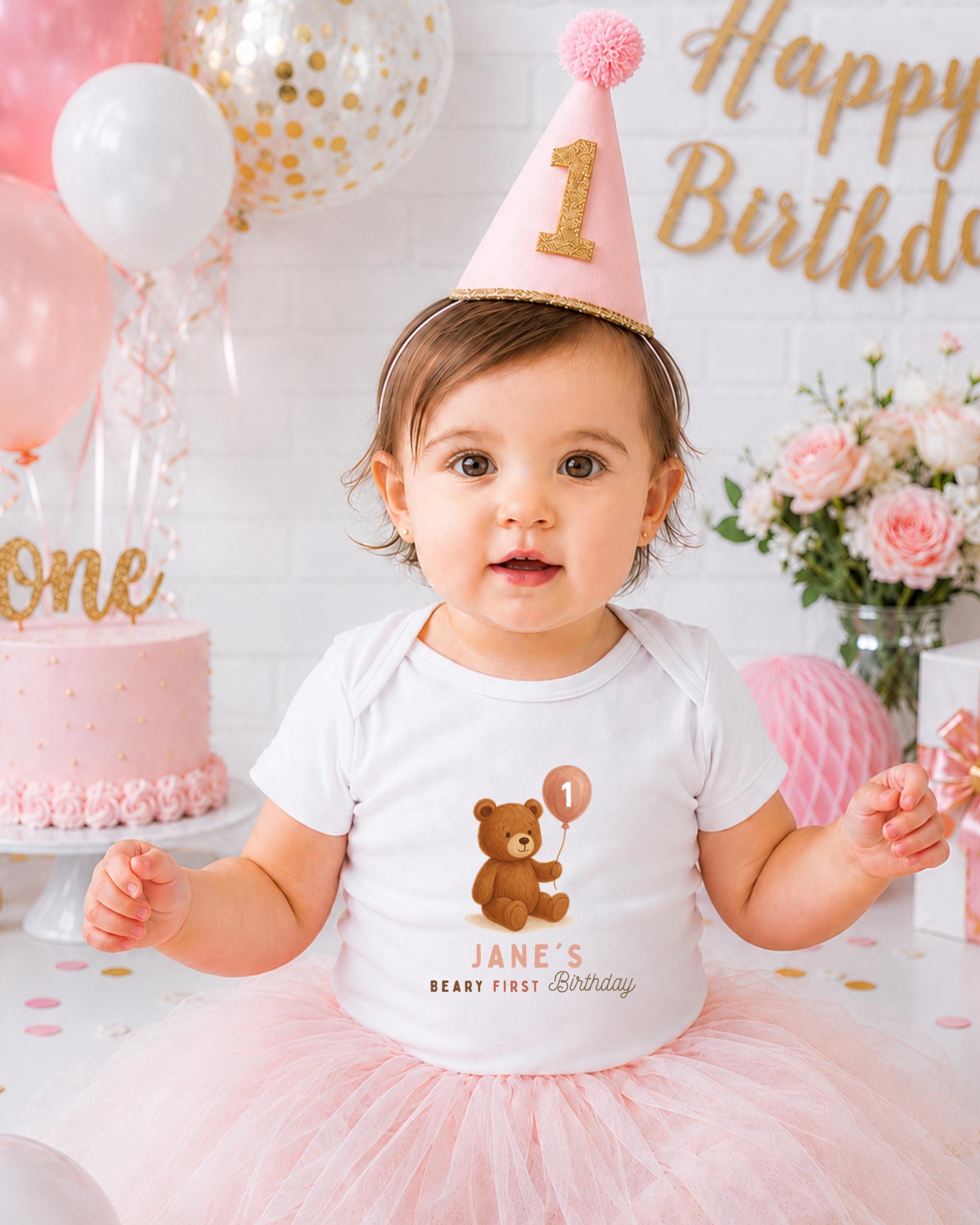 A young girl wearing a birthday hat and a t-shirt with a teddy bear on it, surrounded by balloons and a cake, celebrating her first birthday.