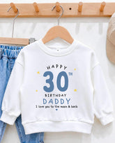 A white sweatshirt with a birthday message printed on it, hanging on a wooden hanger.