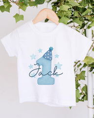 A white t-shirt with a blue number one and stars printed on it, hanging on a wooden hanger.
