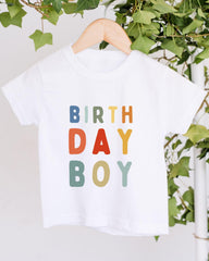 A white t-shirt with the text "BIRTHDAY BOY" printed on it in a colorful, playful font.