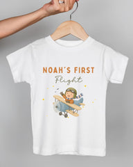 A white t-shirt with a cartoon image of a boy in a pilot's suit and helmet, along with the text "Noah's first flight" printed on it.