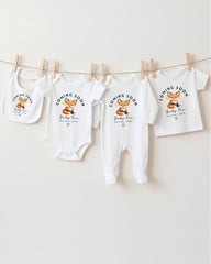 A row of white baby clothes with the text "Coming Soon Baby Fox December 2016" printed on them, along with a small image of a fox.