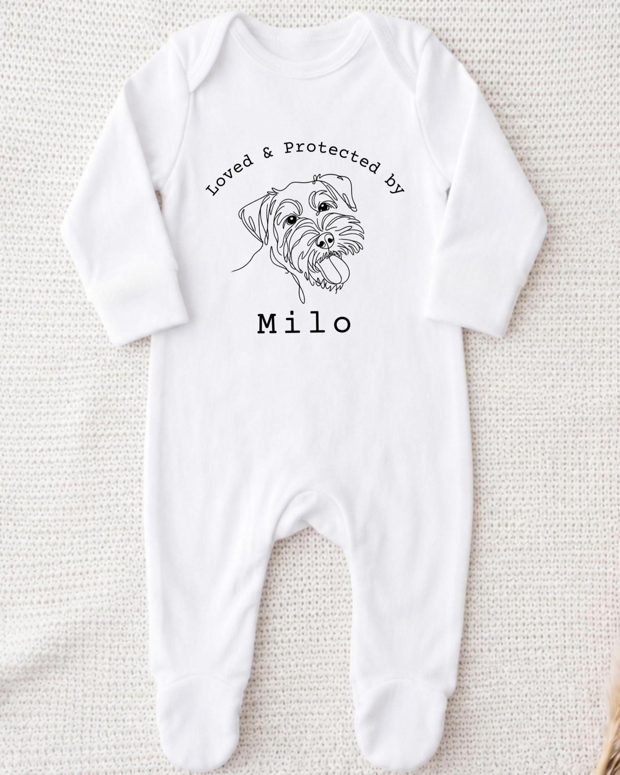 A white onesie with a black line drawing of a dog's face and the text "Loved & Protected by" above it, along with the name "Milo" below the drawing.