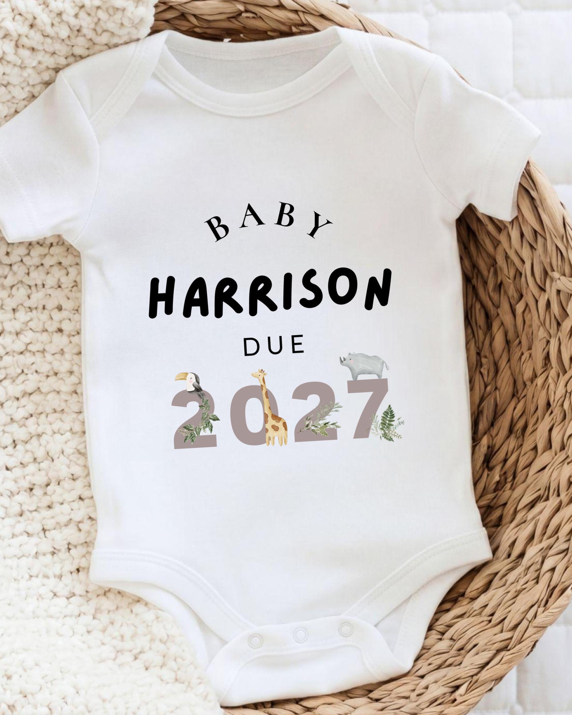 A white baby onesie with text printed on it, placed on a woven basket.