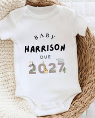 A white baby onesie with text printed on it, placed on a woven basket.