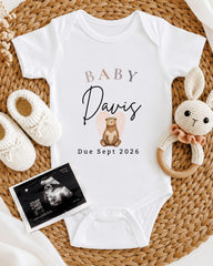 A baby's onesie with the name "Baby Davis" printed on it, along with a crocheted rabbit toy and a baby bootie. There is also an Ultrasound image of a baby's belly.