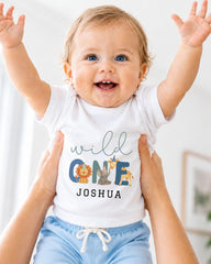 A smiling baby wearing a white t-shirt with a personalized name and animal designs, being held up by someone's arms.