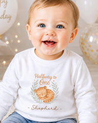 A smiling baby boy wearing a white shirt with a graphic of a cat and the text "Halfway to One - Shepherd" printed on it.