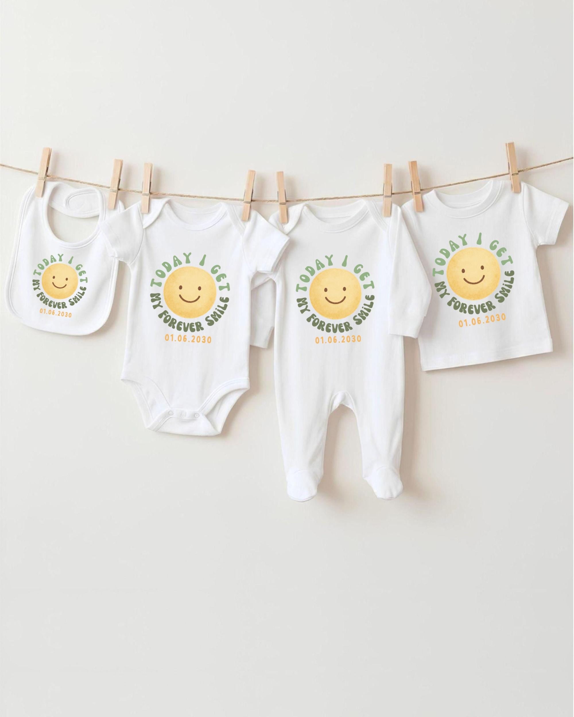A row of four white baby clothes with a cheerful smiley face design, hanging on a clothesline.